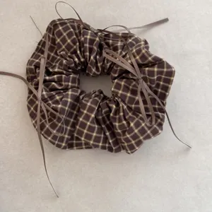 Close-up of vintage brown plaid scrunchie with decorative ribbons on grey background