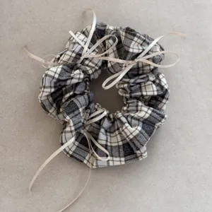 Close-up detail of retro dark plaid scrunchie featuring multiple beige ribbon bows