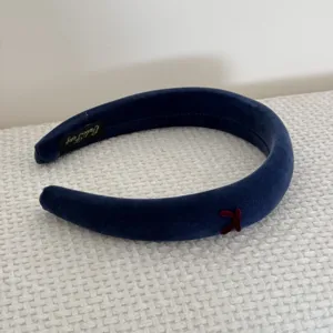Close-up detail of a navy blue velvet padded headband featuring a red bow accent