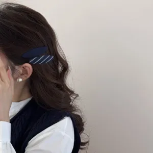 Dettaglio di fermagli in tessuto blu navy e a righe su capelli castani ondulati.