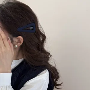 Dettaglio della clip per capelli triangolare in tessuto minimalista indossata di lato