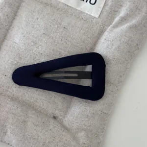 Vista dettagliata di una clip per capelli BB a triangolo in tessuto blu navy su fondo beige.