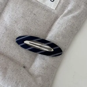 Dettaglio di un fermaglio per capelli in tessuto a righe blu navy su sfondo trapuntato