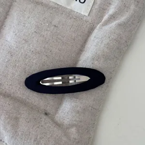 Primo piano di un fermaglio per capelli ovale in tessuto blu navy su tessuto beige