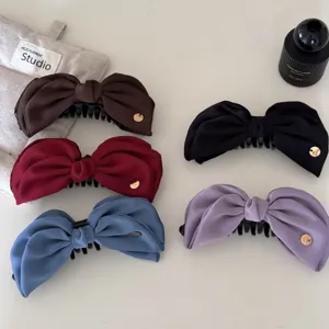 Detailed macro view of satin bow banana clips in five elegant colors on a desk.