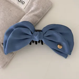 Close-up of elegant blue satin bow hair banana clip on beige canvas background