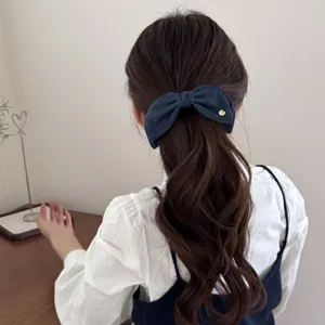 Close-up detail showing a vintage blue denim bow banana clip on a wavy ponytail
