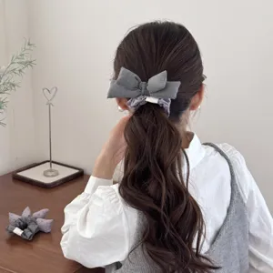 Back view of a person wearing a stylish grey padded bow hair scrunchie on a long wavy ponytail