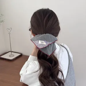 Detailed view of a vintage padded grey hair scrunchie featuring red piping and sewn label