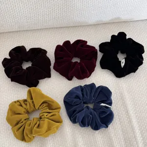 Close-up of assorted vintage velvet scrunchies in deep fall colors on white texture.
