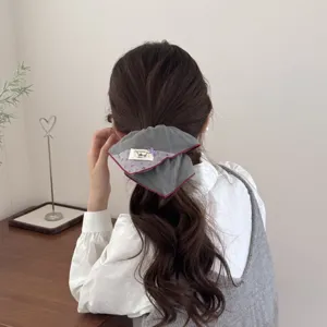 Detail of a gray vintage padded scrunchie with a floral tag worn on a ponytail hair