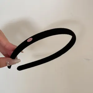 Close-up of a black suede narrow headband featuring a small pink 'Love' patch detail