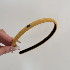 Close-up detail of a mustard yellow suede thin headband with a small blue decorative plaque