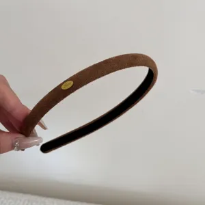 Macro view of a minimalist brown suede headband with a decorative gold Love tag detail