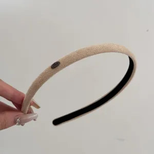 Detailed view of a minimalist beige suede narrow headband featuring a small 'Love' metal tag