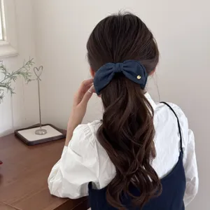 Detail shot of a vintage denim blue bow banana hair clip on a wavy brown ponytail.