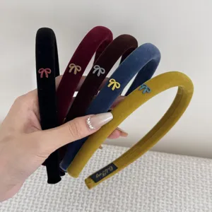 Detail view of five colorful velvet headbands with delicate bow accents held in hand.