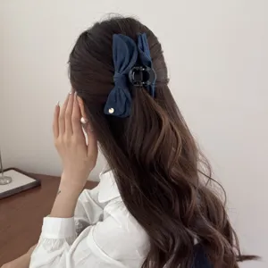 Close-up of a denim bow banana hair clip worn by a woman with long wavy hair