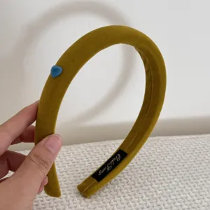 Vue détaillée d'un serre-tête en velours jaune moutarde avec petit cœur bleu décoratif