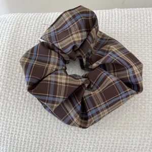 Detailed close-up of a retro brown and blue plaid scrunchie on textured white fabric