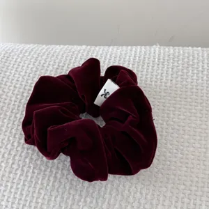 Close-up of a vintage burgundy velvet scrunchie with a minimalist white logo tag.