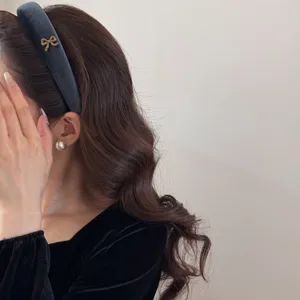 Elegant dark velvet wide headband with a gold bow accent worn by a model with wavy hair