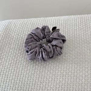 Detailed view of a purple floral scrunchie hair tie on white textured fabric background