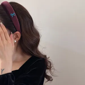 Elegant burgundy velvet wide headband with a small blue bow accent worn by a model