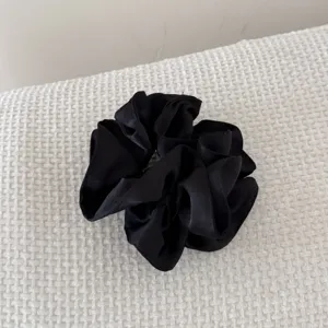 Gros plan d'un chouchou en satin noir plissé à double épaisseur sur fond texturé blanc