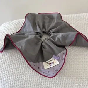 Detail view of a retro grey oversized scrunchie with burgundy piping and dog tag.
