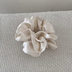 Détail d'un chouchou en satin plissé double couche crème sur fond de tissu texturé