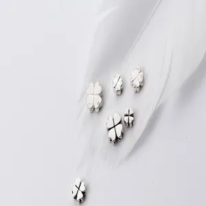 Close-up of S925 silver four-leaf flower spacer beads on a soft white feather background.