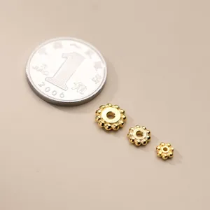 Distanziatori a fiore in argento S925 placcato oro in tre misure accanto a una moneta