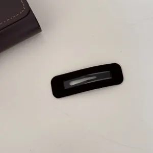 Gros plan d'une pince à cheveux rectangulaire en velours marron foncé sur fond blanc