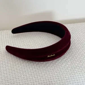 Dettaglio ravvicinato di un cerchietto in velluto bordeaux imbottito con targhetta Handmade