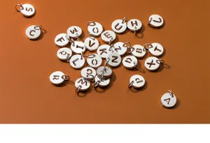 Macro detail of S925 sterling silver hollowed alphabet letter round charms for DIY jewelry.