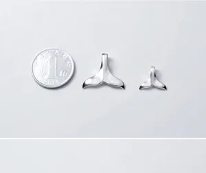 Dettaglio di due ciondoli a coda di balena in argento 925 lucido mostrati con moneta di scala.