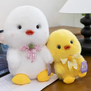 Two cute white and yellow plush duck toys with plaid bows sitting next to a laptop