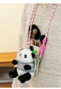 Primer plano de un colgante de peluche de panda con jersey gris y correa rosa para móvil.