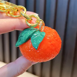 Realistic resin orange keychain with green leaves and a gold-colored metal link ring.