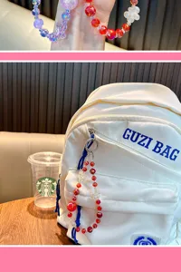 Close-up of a red flower beaded crystal charm hanging on a white canvas backpack