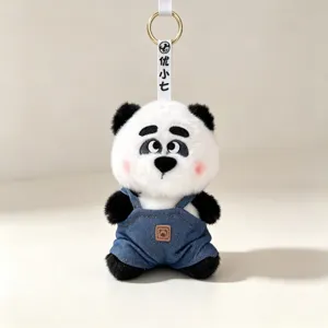 Detail view of a cute plush panda keychain charm wearing blue denim overalls and golden ring