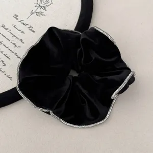 Close-up detail of a black velvet scrunchie featuring elegant sparkling rhinestone edges