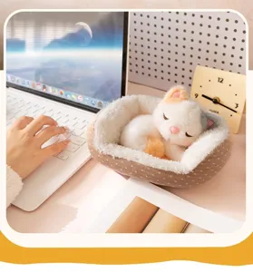 Peluche de gato realista durmiendo en una pequeña cama sobre un escritorio de oficina