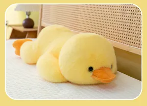 Adorable soft yellow duck plush toy lying prone on a bed, cozy bedroom detail shot.