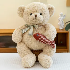 Süßer Teddybär aus Plüsch mit Lockenfell hält ein rotes Fisch-Ornament