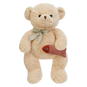 Süßer beiger Teddybär aus Plüsch mit Schleife und kleinem gestreiftem Fisch auf weißem Hintergrund