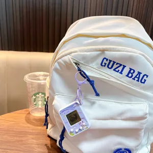 Handheld electronic pet game machine keychain attached to a white canvas backpack