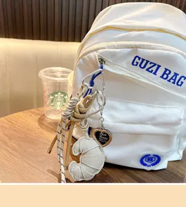 Close-up of a white padded leather croissant keychain charm on a white backpack.