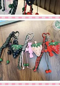 Detail of three strawberry leather keychains in black, pink, and red with braided ropes.